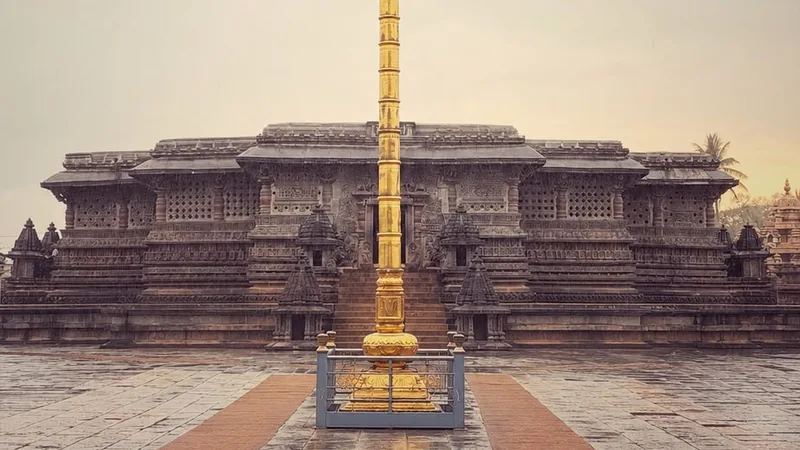 The Chennakeshava temple at Belur across a rain-wet courtyard, a gilded pillar standing before the carved facade