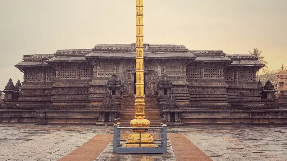 The Chennakeshava temple at Belur across a rain-wet courtyard, a gilded pillar standing before the carved facade