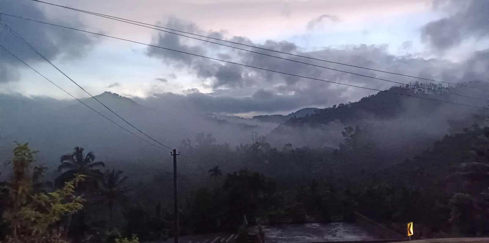 Cloud lying in a wooded valley at dawn, with ridges behind, seen from the forecourt wall of the homestay