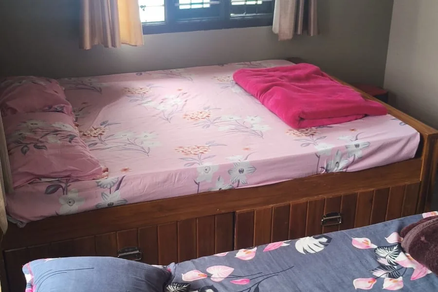 A double bed with floral bedding beside a curtained window with a grille, and a second bed in the foreground